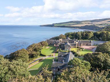 A coastal estate with multiple stone buildings surrounded by green lawns and trees overlooking the sea at Ardlochan Lodge - Culzean Castle in Maybole