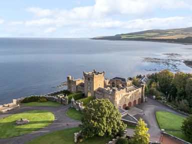 An aerial view of a castle by the sea with surrounding greenery and a paved driveway at Ardlochan Lodge - Culzean Castle in Maybole