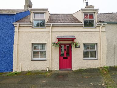 A small house with a red door and two windows on either side at Angorfa in Beaumaris