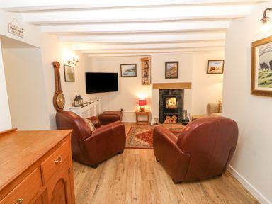 A living room with two leather armchairs a fireplace and a wall-mounted TV at Angorfa in Beaumaris