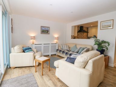 A living room with beige leather sofas a small wooden table lamps and paintings at Angorfa in Beaumaris