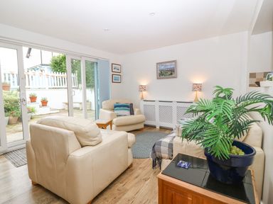 A living room with cream sofas a blue plant pot on a wooden table and sliding glass doors leading outside at Angorfa in Beaumaris
