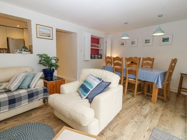 A living room with a white armchair and sofa and a wooden dining table with chairs at Angorfa in Beaumaris