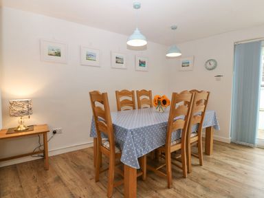 A dining room with a wooden table covered with a blue polka dot tablecloth and six wooden chairs at Angorfa in Beaumaris