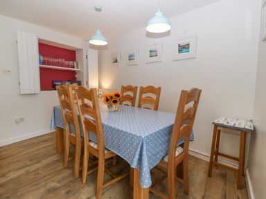 A dining room with a wooden table covered with a blue polka dot tablecloth and six wooden chairs at Angorfa in Beaumaris