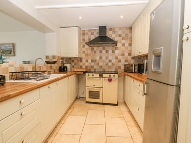 A kitchen with cream cabinets wooden countertops a tiled backsplash a cream oven a stainless steel fridge and a stainless steel sink at Angorfa in Beaumaris