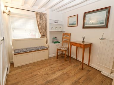 A room with wooden flooring a bench with cushions a wooden chair a small table two framed paintings and shelves with decorative items at Angorfa in Beaumaris