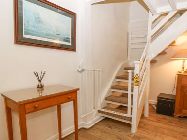 A staircase with carpeted steps a wooden table with a glass top and a reed diffuser a framed painting on the wall and a wooden cabinet with a lamp in a hallway at Angorfa in Beaumaris