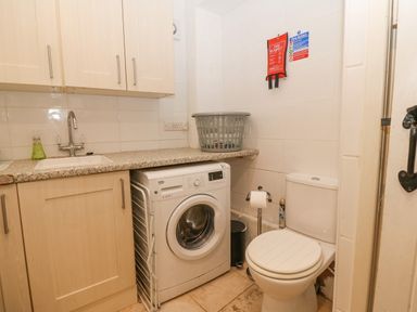 A utility room with a washing machine a toilet a sink and cabinets at Angorfa in Beaumaris