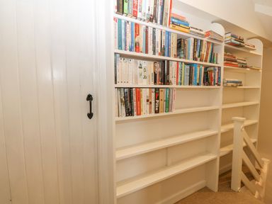 A white bookshelf filled with books next to a white wooden door with a black handle at Angorfa in Beaumaris