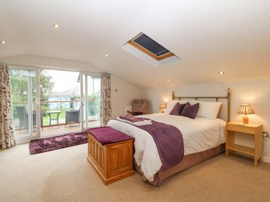 A bedroom with a bed wooden chest bedside tables lamps and sliding glass doors leading to a balcony at Angorfa in Beaumaris