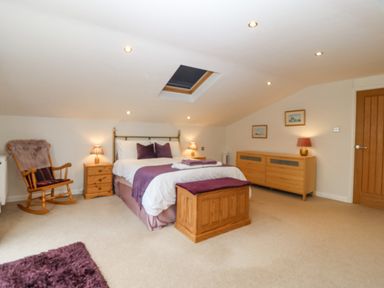 A bedroom with a bed a rocking chair a wooden chest and a wooden dresser at Angorfa in Beaumaris