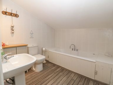 A bathroom with a sink, toilet, bathtub, wooden floor, and wall hooks at Angorfa in Beaumaris