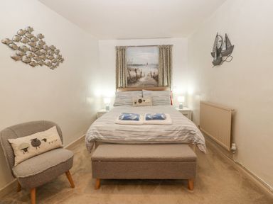 A bedroom with a bed and decorative pillows a chair with a pillow wall art of fish and boats at Angorfa in Beaumaris