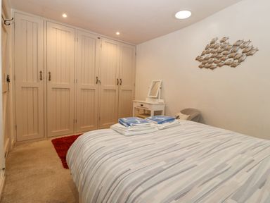 A bedroom with a bed striped bedding folded towels on the bed a white vanity table wall art of fish and built-in wardrobes at Angorfa in Beaumaris