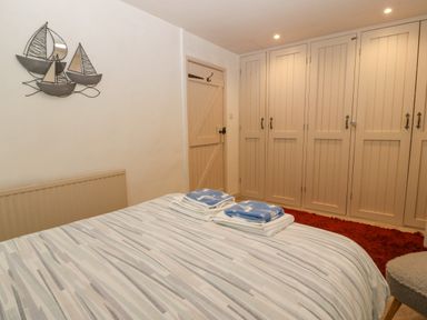 A bedroom with a bed covered in striped bedding towels on the bed built in wardrobes a red rug and a wall decoration of boats at Angorfa in Beaumaris