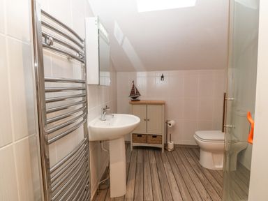 A bathroom with a sink a towel radiator a cabinet with a sailboat decoration a toilet and wooden flooring at Angorfa in Beaumaris