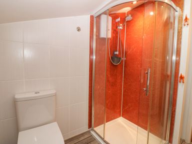 A bathroom with a toilet and a glass enclosed shower with red walls at Angorfa Beaumaris