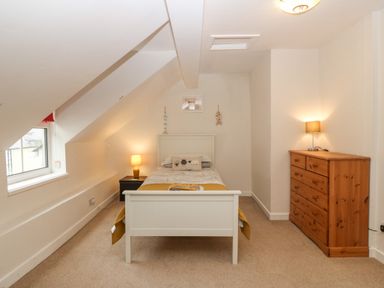 A bedroom with a single bed nightstand with lamp wooden dresser with lamp and a window at Angorfa in Beaumaris