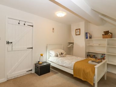 A bedroom with a single bed a bedside table with a lamp a white wooden door and shelves with books and a basket at Angorfa in Beaumaris