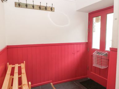 An entryway with a pink door and pink wooden paneling a wooden shoe rack and wall hooks at Angorfa in Beaumaris