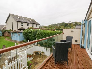 A balcony with two wicker chairs and glass railing overlooking a garden with plants and a blue shed at Angorfa in Beaumaris