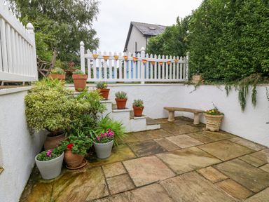 A small paved patio garden with potted plants white walls a stone bench and a white picket fence at Angorfa in Beaumaris