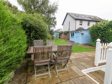 An outdoor patio with wooden table and chairs next to a garden and a building with blue walls at Angorfa in Beaumaris