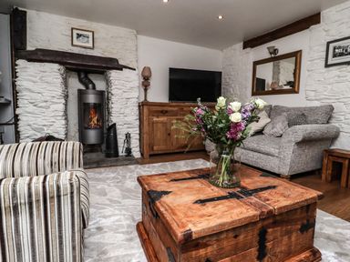 A living room with a stone fireplace wooden coffee table with flowers striped armchair and grey sofa at Garretts in Kingsand And Cawsand