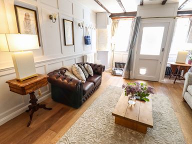 A living room with a brown leather sofa and cushions a wooden coffee table with flowers and side tables with lamps at Garretts in Kingsand And Cawsand