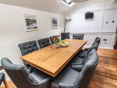 A dining room with wooden table and gray chairs with paintings on the wall at Garretts in Kingsand And Cawsand