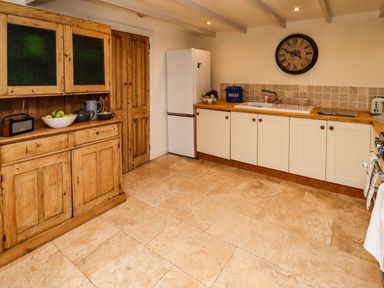 A kitchen with wooden cabinets a refrigerator a sink and a wall clock at Garretts in Kingsand And Cawsand