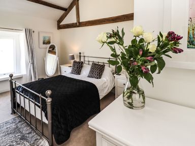 A bedroom with a metal bed frame black blanket two bedside tables a standing mirror and a vase of flowers on a dresser at Garretts Kingsand And Cawsand