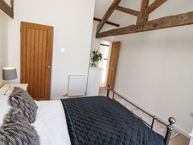 A bedroom with a bed with black quilt and fur pillows a side table with lamp wooden doors exposed beams and flowers on a small cabinet at Garretts Kingsand And Cawsand