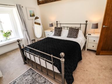 A bedroom with a metal bed frame black blanket white bedding two bedside tables with lamps a standing mirror window with curtains and a flower vase at Garretts in Kingsand And Cawsand