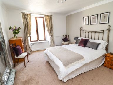 A bedroom with a double bed curtains on a window chairs and a wooden dresser at Garretts in Kingsand And Cawsand