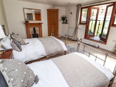 A bedroom with two beds a wooden door a fireplace and open windows at Garretts in Kingsand And Cawsand