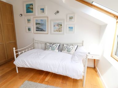 A bedroom with a white metal bed, wooden floor, framed pictures on the wall, and a wooden wardrobe at Garretts Kingsand And Cawsand