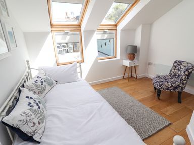 A bedroom with a white bed frame pillows a small side table with a lamp a patterned chair and two skylight windows at Garretts in Kingsand And Cawsand