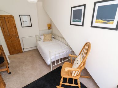 A bedroom with a single bed a wooden rocking chair with a cushion a wooden door and framed pictures on the walls at Garretts Kingsand And Cawsand
