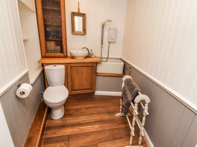 A bathroom with a toilet wooden cabinet a sink a shower and a towel rack with towels at Garretts in Kingsand And Cawsand