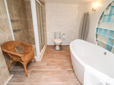 A bathroom with a bathtub a toilet a shower enclosure a wicker chair and a towel rack at Garretts Kingsand And Cawsand