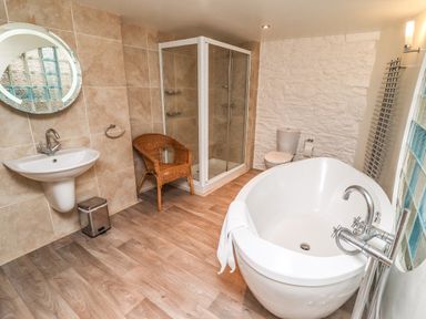 A bathroom with a freestanding bathtub sink toilet shower and wicker chair at Garretts in Kingsand And Cawsand