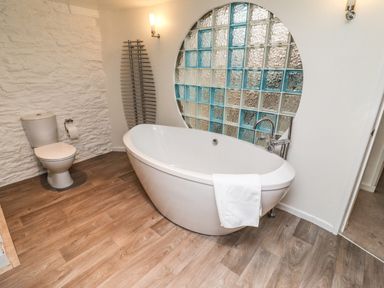 A bathroom with a toilet a freestanding bathtub and a textured window at Garretts in Kingsand And Cawsand