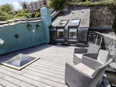An outdoor wooden deck with two wicker chairs a skylight windows on a sloped roof and planters attached to a blue wall at Garretts in Kingsand And Cawsand