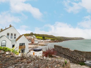A coastal village with white houses stone walls and a clock tower by the sea at Garretts Kingsand And Cawsand