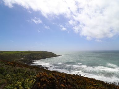 A coastal landscape with cliffs, green fields, and waves crashing on rocky shore at Garretts in Kingsand And Cawsand