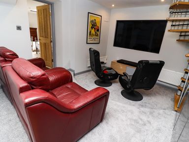 A living room with red leather sofas two black swivel chairs a large wall mounted television a wooden media console a rugby poster on the wall and a spiral staircase at Garretts in Kingsand And Cawsand
