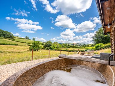 A hot tub overlooking a grass field and hills at Birch Banc Retreats - Bedw Llanidloes
