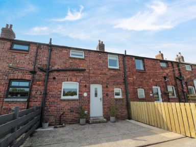A brick terraced house with white door and windows and fenced front yards at The Miners Cottage in Scremerston near Berwick-Upon-Tweed